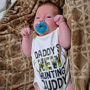 Noah is registered to the contest to win money with this photo: baby, infant, pacifier, onesie, blanket, lying_down, face, expression, cute, child, newborn, clothing, human, skin, hand, fist, blue, brown, pattern, portrait