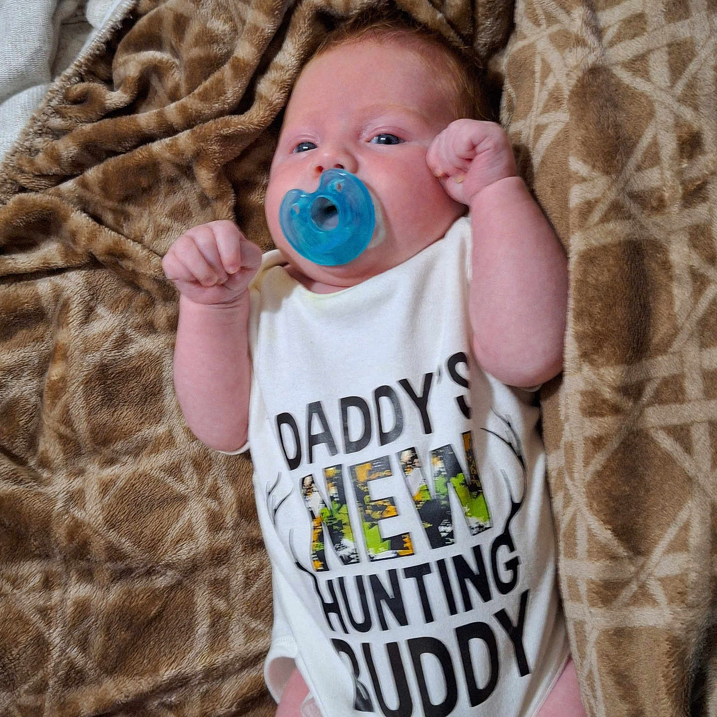 Noah is registered to the contest to win money with this photo: baby, blanket, blue, brown, child, clothing, cute, expression, face, fist, hand, human, infant, lying_down, newborn, onesie, pacifier, pattern, portrait, skin