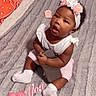 baby, infant, child, sitting, blanket, headband, flower, phone, drool, pink_shorts, white_shirt, socks, pillow, orange_bandana, bed, indoor, cute, curious_expression, home, soft_texture