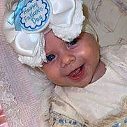 Darla-Marie is registered to the contest to win money with this photo: baby, infant, smiling, face, blue_eyes, white_bow, lace_dress, ribbon, blanket, fabric, closeup, portrait, cute, happy, child, headwear, soft_texture, indoors, celebration, holiday