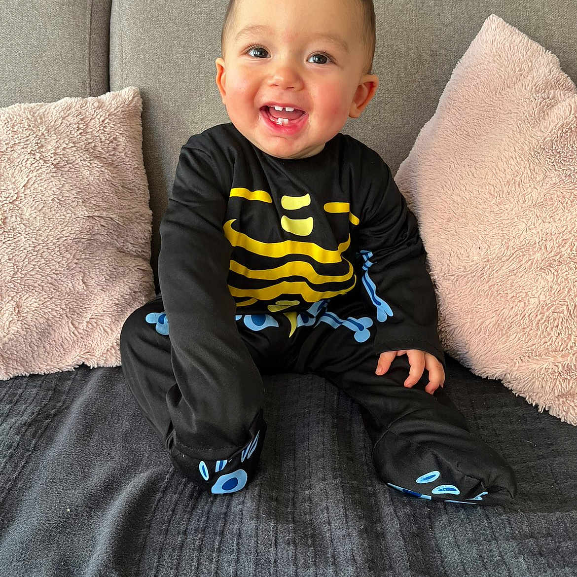 Waël participe au concours pour gagner de l'argent avec cette photo : baby, black_clothing, child, clothing, couch, cute, face, happy, head, home_interior, indoors, joyful, person, pink_pillows, sitting, skeleton_costume, smiling, soft_texture, toddler, young_child