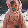 baby, child, pacifier, pink_clothing, onesie, headband, bow, bear_design, quilt, sitting, indoor, soft_light, cute, portrait, infant, face, eyes, cozy, plush, floor