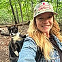 woman, cat, outdoor, forest, backpack, denim_jacket, cap, smile, nature, pet, animal, happy, walking, leaf, tree, adventure, exploring, daylight, casual, portrait