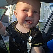 Asher is registered to the contest to win money with this photo: baby, child, infant, smiling, tongue_out, pacifier_clip, black_clothing, car_interior, sunlight, shadow, face, cheeks, short_hair, person, outdoor, window, seat, door, playful, cute