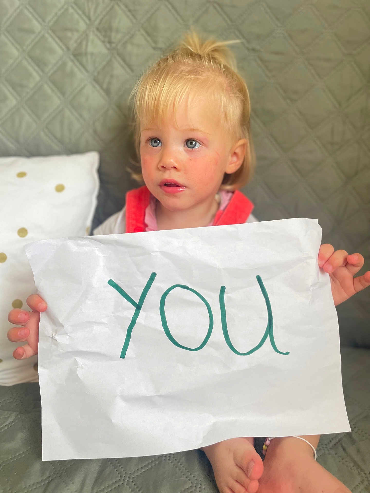 Mia participe au concours pour gagner de l'argent avec cette photo : child, toddler, blonde_hair, blue_eyes, paper, handwriting, couch, quilted, sitting, indoor, curious, expression, casual_clothing, holding, feet, pillow, home, furniture, face, person
