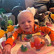 Daxton joined the competition — help win amazing prizes! baby, child, infant, smiling, playtime, toy, activity_center, orange_clothing, indoor, furniture, blanket, frog_toy, fish_toy, happy, face, person, head, colorful, couch, living_room