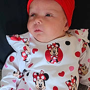 Phoebe is registered to the contest to win money with this photo: baby, infant, headband, red_bow, minnie_mouse, cartoon, pattern, white_shirt, red_hearts, lying_down, child, cute, clothing, portrait, closeup, face, expression, indoor, textile, fabric