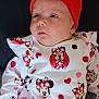 baby, infant, headband, red_bow, minnie_mouse, cartoon, pattern, white_shirt, red_hearts, lying_down, child, cute, clothing, portrait, closeup, face, expression, indoor, textile, fabric