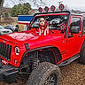 adventure, animal, dog, fence, four_wheel_drive, gravel, hood, jeep, light, offroad, outdoor, parked_car, pet, red_vehicle, sky, sweater, tire, tree, vehicle, winter