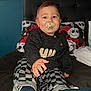 baby, pacifier, child, bed, sweater, checkered_pants, sock, headboard, photo_wall, blue_wall, hand, infant, indoor, portrait, cozy, curious, reaching, clothing, young_child, cute