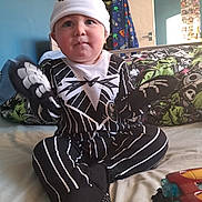 Hunter-James is registered to the contest to win money with this photo: baby, child, costume, jack_skellington, nightmare_before_christmas, bed, bedding, clothing, hat, gloves, indoor, person, cute, sitting, toy, room, wall, door, coat, playful