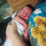 Maggie joined the competition — help win amazing prizes! newborn, baby, infant, sleeping, face, portrait, blanket, swaddled, adult_hand, caregiver, nasal_tube, medical_care, cuddling, close_up, indoor, wooden_background, floral_shirt, blue_clothing, peaceful, family