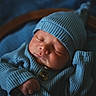 newborn, baby, sleeping, portrait, knit_hat, mittens, blue_clothing, swaddled, peaceful, face, closed_eyes, infant, cozy, bed, blanket, indoor, soft_lighting, close_up, button, photography