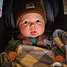 baby, infant, child, car_seat, beanie, blanket, pacifier, portrait, face, eyes, wide_eyed, looking_at_camera, seated, bundled, warm_clothing, car_interior, safety_harness, cozy, close_up, photograph