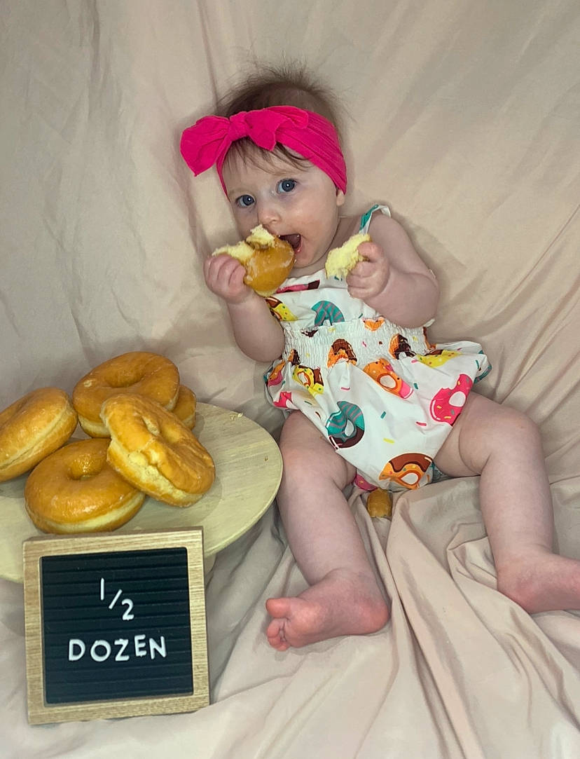 Everleigh is registered to the contest to win money with this photo: arm, baby_toddler_clothing, baking, child, comfort_food, doll, dress, fawn, finger_food, gluten, hand, headwear, ingredient, junk_food, person, pink, plush, sitting, stuffed_toy, teddy_bear