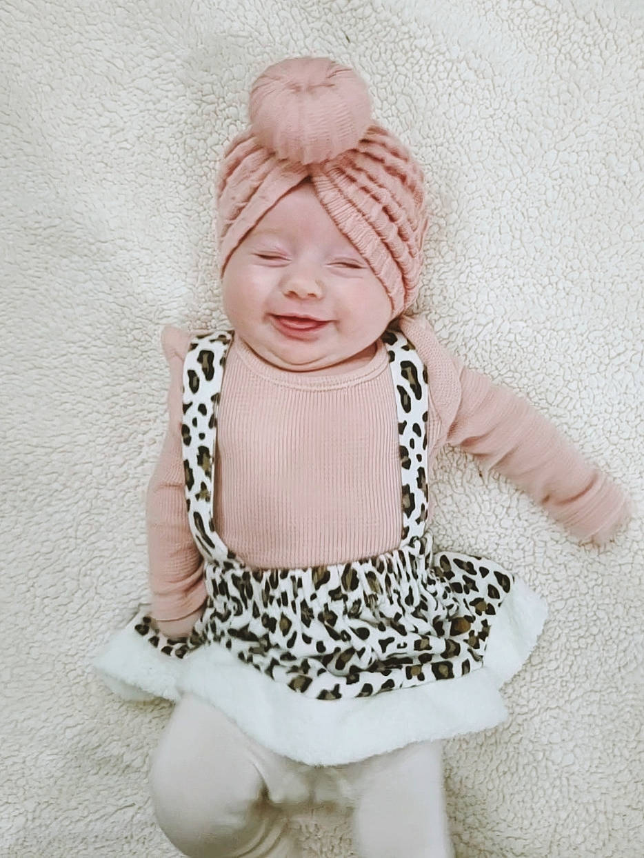 Sutton is registered to the contest to win money with this photo: arm, baby, baby_toddler_clothing, cap, costume_hat, face, fashion_design, happy, head, headgear, headwear, jewellery, knit_cap, neck, necklace, pattern, person, sleeve, street_fashion, toddler