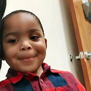 Carter is registered to the contest to win money with this photo: child, smile, plaid_shirt, indoor, close_up, portrait, dimples, candid, selfie, wooden_door, door_handle, wall, collar, button, short_hair, toddler, happy, casual_clothing, face, playful_expression