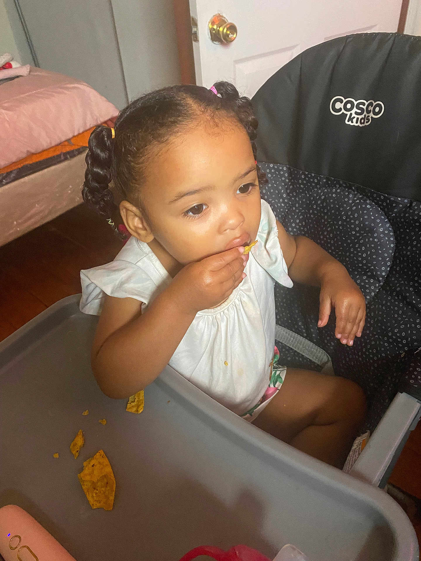 Legacy is registered to the contest to win money with this photo: toddler, child, high_chair, food, snack, chip, braided_hair, indoor, room, door, bed, tray, crumbs, clothing, person, eating, young_child, cosco_kids, hair_ties, furniture