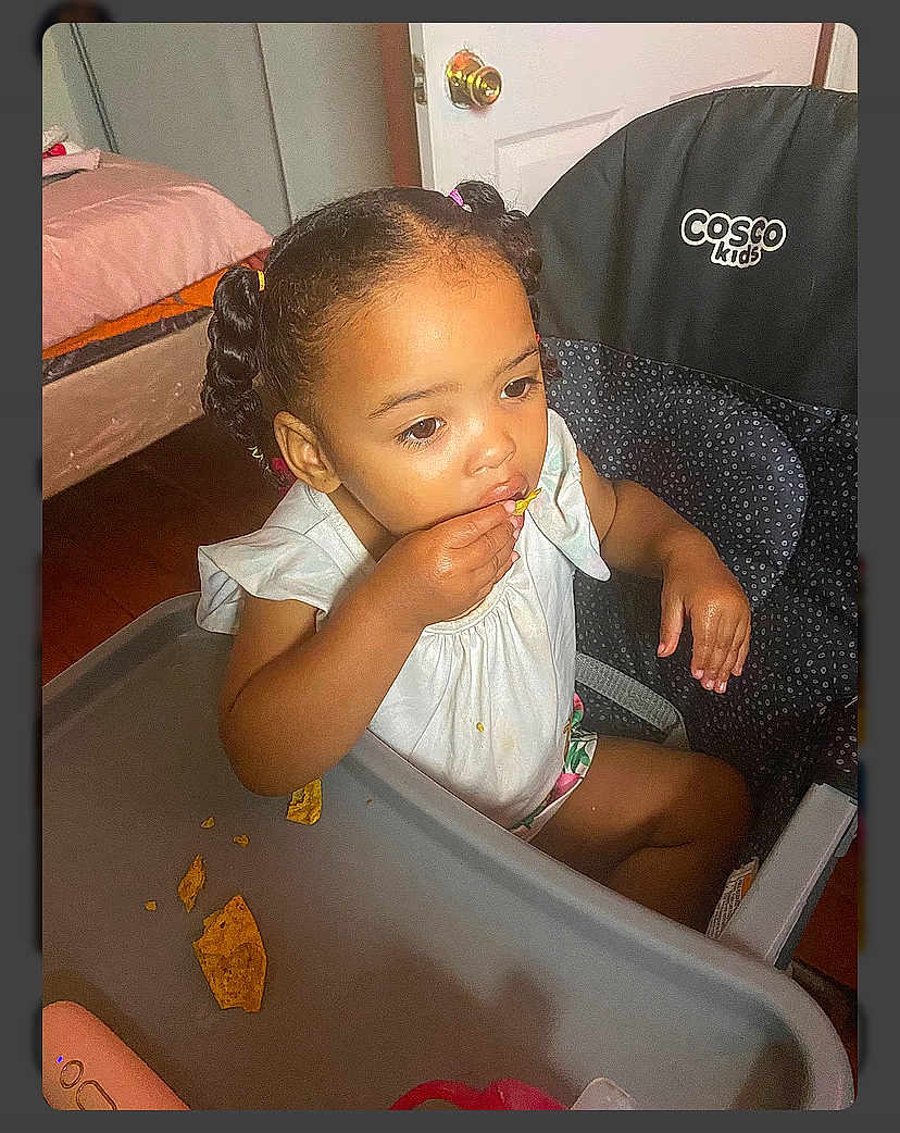 Legacy joined the competition — help win amazing prizes! child, toddler, highchair, eating, snack, tortilla_chips, crumbs, hand, face, braided_hair, pigtails, white_dress, tray_table, indoor, door, doorknob, wood_floor, furniture, brand_logo, portrait