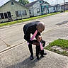 Yasir is registered to the contest to win money with this photo: adult, baby, child, toddler, man, sidewalk, street, suburban, outdoor, daytime, clothing, tie, black_outfit, pink_tie, grass, houses, fence, sky, clouds, footwear