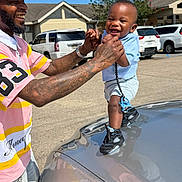 Yasir joined the competition — help win amazing prizes! toddler, man, smiling, tattoos, car, hood, blue_sky, parking_lot, outdoor, holding_hands, child, shorts, sneakers, cap, happy, person, daylight, casual_clothing, buildings, vehicles