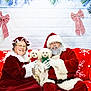 santa_claus, mrs_claus, dog, christmas, holiday, red_couch, snowflake_pattern, festive, smiling, glasses, beard, hat, sweater, gloves, decorations, greenery, bows, portrait, indoor, celebration