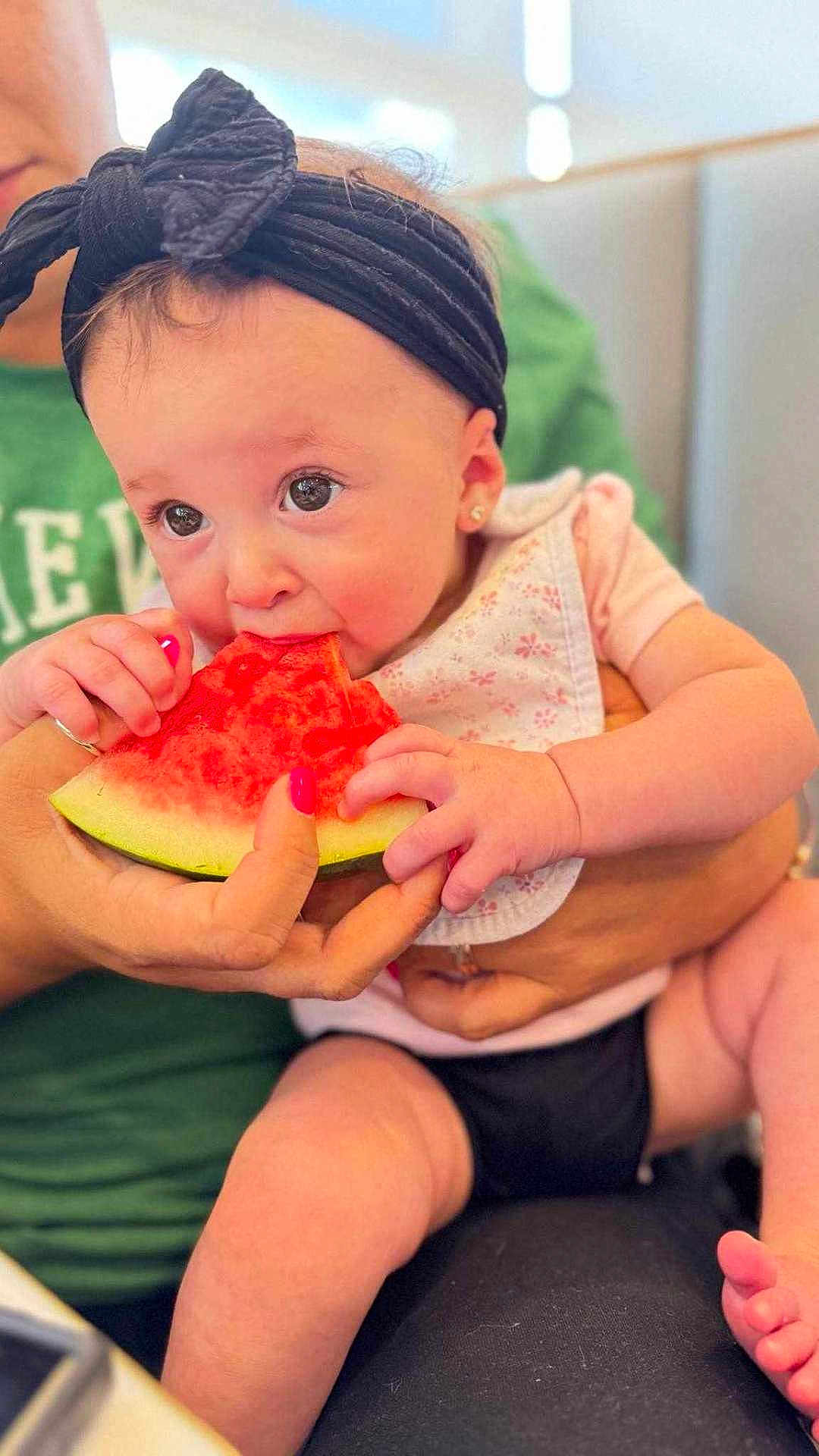 Ariella joined the competition — help win amazing prizes! baby, watermelon, headband, bib, hand, pink_nail_polish, fruit, eating, cute, child, person, skin, clothing, seat, closeup, indoor, holding, food, expression, lap