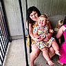Millie-Jean is registered to the contest to win money with this photo: toddler, child, woman, porch, swing, smile, happy, family, outdoor, dress, barefoot, blond_hair, curly_hair, seated, holding, concrete_floor, railing, fence, casual, playful