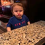 Valerie is registered to the contest to win money with this photo: blue_shirt, bow, child, cute, dark_wood, expression, face, framed_pictures, funny_face, granite_countertop, hair, indoor, lighting, mouth, person, restaurant, sitting, table, toddler, wall_decor