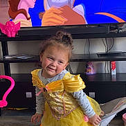 Valerie is registered to the contest to win money with this photo: child, toddler, yellow_dress, princess_costume, smiling, indoor, television, animated_movie, beauty_and_the_beast, toy, floor, furniture, living_room, curly_hair, playful, cute, person, sock, chair, entertainment