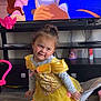 child, toddler, yellow_dress, princess_costume, smiling, indoor, television, animated_movie, beauty_and_the_beast, toy, floor, furniture, living_room, curly_hair, playful, cute, person, sock, chair, entertainment