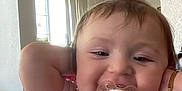 Athena joined the competition — help win amazing prizes! baby, pacifier, pink_shirt, bracelet, indoor, child, smiling, close_up, face, arm, window, natural_light, toy, happy, person, hair, cute, infant, home, relaxed