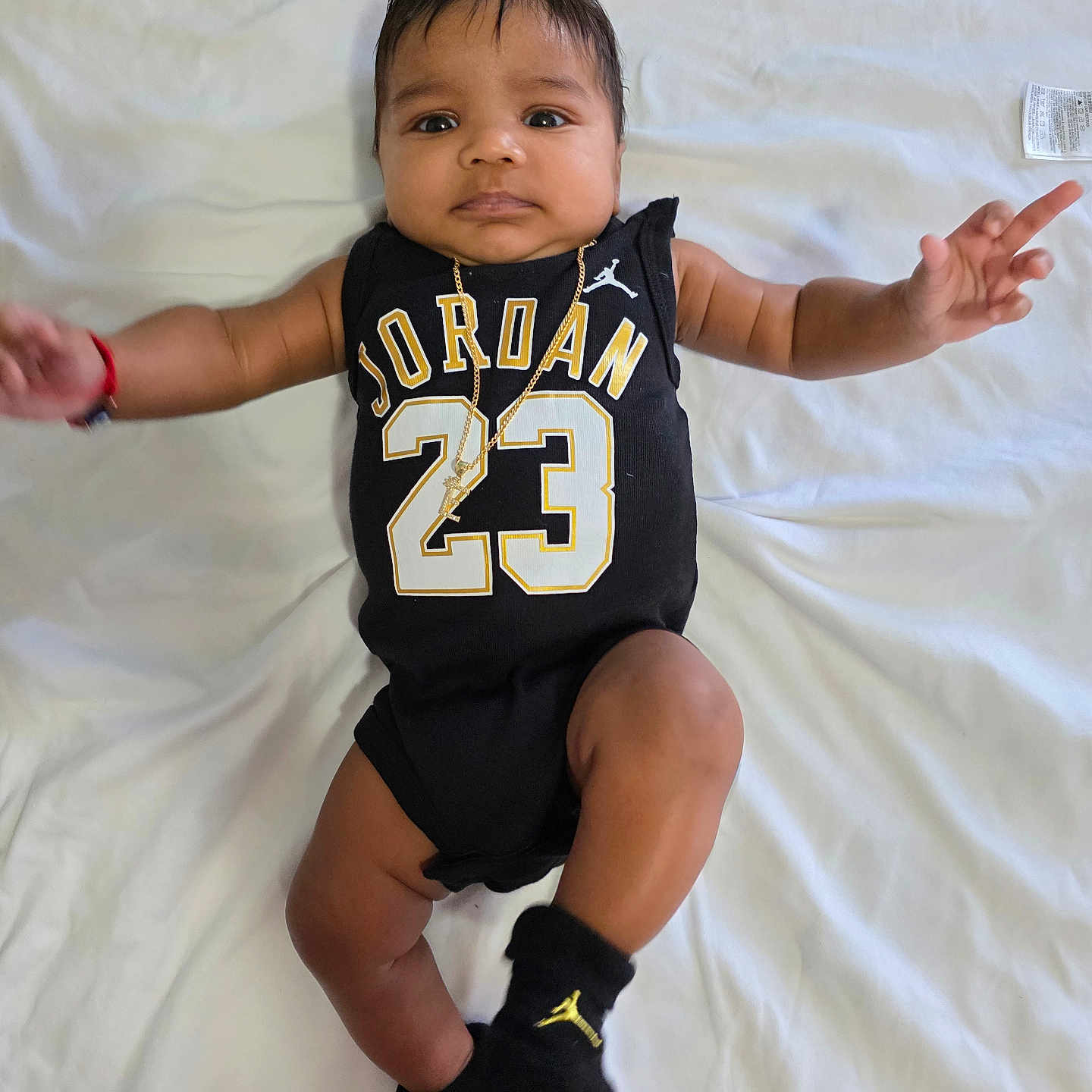 Eithan Zayas Medina is registered to the contest to win money with this photo: baby, child, infant, black_clothing, jordan, number_23, gold_chain, wristband, black_socks, blanket, white_blanket, lying_down, cute, face, arms_outstretched, indoors, portrait, expression, soft_lighting, person