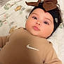 baby, infant, child, headband, bow, nike, clothing, beige_outfit, blanket, animal_print, cute, lying_down, portrait, soft_expression, indoors, curly_hair, fashion, cozy, young_child, person