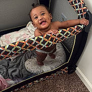 Sariyah joined the competition — help win amazing prizes! baby, playpen, smiling, child, blanket, carpet, indoor, happy, holding, colorful, furniture, person, cute, infant, home, portrait, mesh, standing, young, room