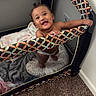 baby, playpen, smiling, child, blanket, carpet, indoor, happy, holding, colorful, furniture, person, cute, infant, home, portrait, mesh, standing, young, room