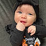 baby, infant, child, face, blue_eyes, headband, bow, black_clothing, orange_skirt, polka_dots, halloween, pumpkin, cute, smile, hand_in_mouth, couch, fabric, portrait, indoors, person