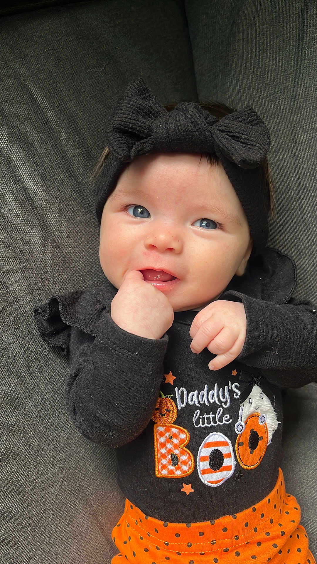 Emiliana is registered to the contest to win money with this photo: baby, infant, child, face, blue_eyes, headband, bow, black_clothing, orange_skirt, polka_dots, halloween, pumpkin, cute, smile, hand_in_mouth, couch, fabric, portrait, indoors, person
