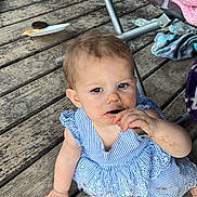 Scarlett is registered to the contest to win money with this photo: toddler, child, messy, blue_dress, striped_dress, wooden_deck, floor, barefoot, spoon, food_stains, face, hand, legs, chair, blanket, fabric, outdoor, playful, person, candid