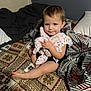 Scarlett is registered to the contest to win money with this photo: toddler, child, bed, blanket, pillow, clothing, indoor, person, wall, pattern, fabric, cute, baby, sitting, holding, soft, comfort, room, portrait, young