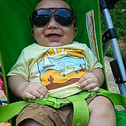 George is registered to the contest to win money with this photo: baby, child, sunglasses, stroller, green, tshirt, shorts, smile, happy, outdoor, grass, seatbelt, person, infant, summer, sunny, cute, casual, clothing, portrait