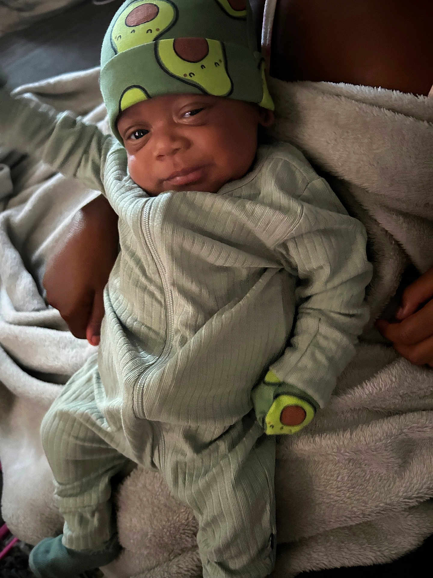 Travis is registered to the contest to win money with this photo: baby, infant, avocado_hat, pajamas, mittens, blanket, soft_texture, smile, sleepy, comfort, child, cute, cozy, hands, footwear, portrait, indoors, warm, relaxed, person