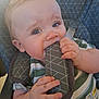 baby, blue_eyes, car_seat, chewing, child, closeup, curious, cute, face, hand, harness, indoor, infant, mischievous, padded_strap, seatbelt, sitting, soft_lighting, striped_shirt, young_child