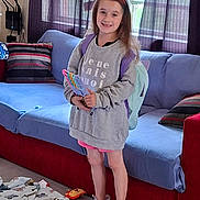 Scarlett joined the competition — help win amazing prizes! child, girl, smiling, indoor, sofa, backpack, pop_it_toy, sneakers, sweatshirt, curtains, pillows, window, blanket, floor, toy, casual_clothing, home, daylight, happy, person