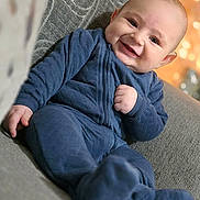 Qais Alhamwi is registered to the contest to win money with this photo: baby, smiling, blue_outfit, couch, indoor, happy, child, portrait, face, infant, sitting, cozy, warm_lighting, blurred_background, cute, young_child, soft_texture, relaxed, comfort, casual_clothing