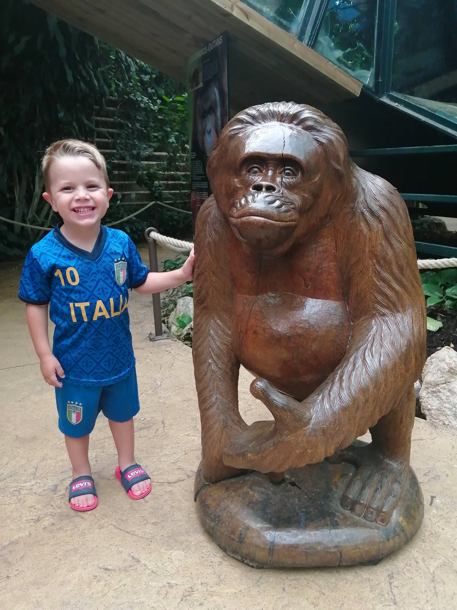 Tizio participe au concours pour gagner de l'argent avec cette photo : art, fun, fur, grass, human, joy, lawn_ornament, leisure, person, plant, primate, recreation, sculpture, shorts, sitting, smile, snout, statue, temple, terrestrial_animal