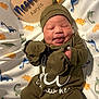 Nessiah is registered to the contest to win money with this photo: baby, baby_mittens, blanket, child, clothing, cute, dinosaur_pattern, green_outfit, hat, indoors, infant, lying_down, name_sign, newborn, person, portrait, sleepy, smiling, soft_lighting, wooden_sign