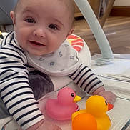 Cody is registered to the contest to win money with this photo: baby, child, rubber_duck, toy, smiling, indoor, floor, striped_clothing, bib, glass_container, furniture, wood_floor, playtime, infant, cute, happy, closeup, person, baby_toys, crawling