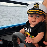 Brantley Tharpe is registered to the contest to win money with this photo: baby, captain_hat, boat, steering_wheel, water, lake, cloudy_sky, child, person, outdoor, black_shirt, hand, face, young_child, nautical, transportation, summer, cute, portrait, expression