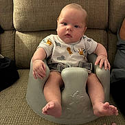 Bryce is registered to the contest to win money with this photo: baby, child, infant, baby_seat, couch, fabric, onesie, animal_print, hand, indoor, person, seated, curious_expression, plush, soft_lighting, home, furniture, portrait, skin, foot